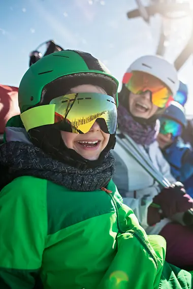 Een gezin zit in een skilift en kijkt lachend uit voor de camera.