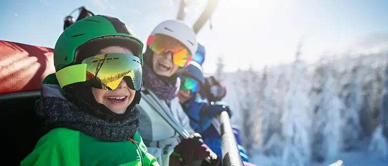 Een gezin zit in een skilift en kijkt lachend uit voor de camera.