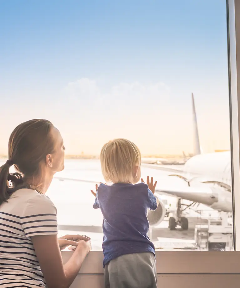 A woman and a child are at the airport and looking out the window at the apron.